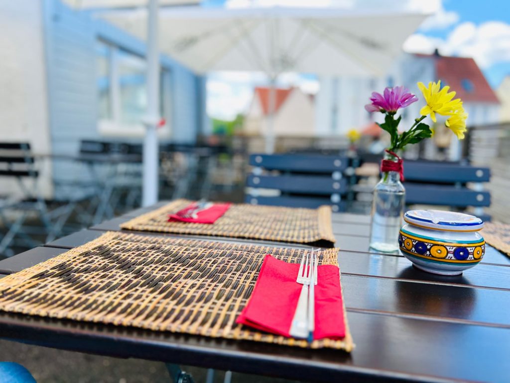 Detailansicht eines mit Platzdecken eingedeckten Biergartentischs in freier sonniger Stadtathmosphäre. Querformat.