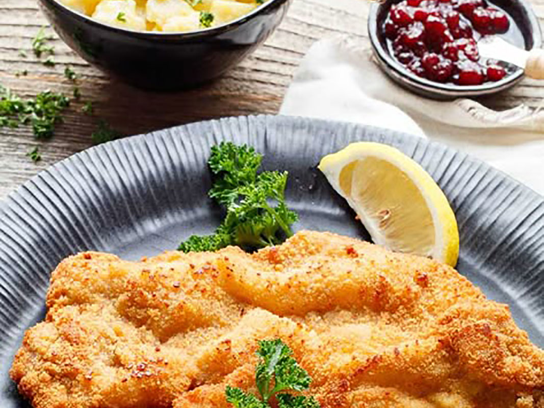 Ausschnitt eines gedeckten Tisches mit einemschwäbischen Kalbsschnitzel im Vordergrund, Kartoffelsalat und Preißelbeeren
