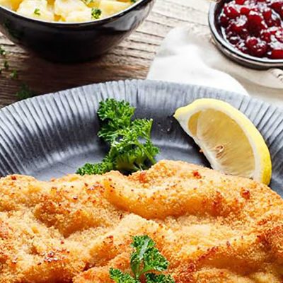 Ausschnitt eines gedeckten Tisches mit einemschwäbischen Kalbsschnitzel im Vordergrund, Kartoffelsalat und Preißelbeeren